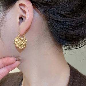 Close-up of a model wearing gold hollow heart hoop earrings with a woven metal texture