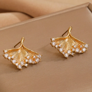 Detail of golden ginkgo leaf earrings with crystal edges on silk background