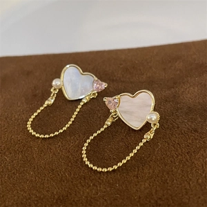 Detailed close-up of heart-shaped shell earrings with pink zircon and gold chain tassels
