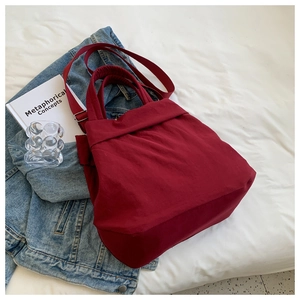 Flat lay of red nylon tote bag on denim jacket with a book and glass decor