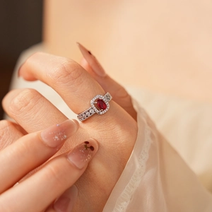 Close-up of elegant silver ring with oval red gemstone and pavé zircon stones on hand