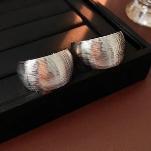 Close-up of silver C-shaped stud earrings with a brushed metal texture on a display