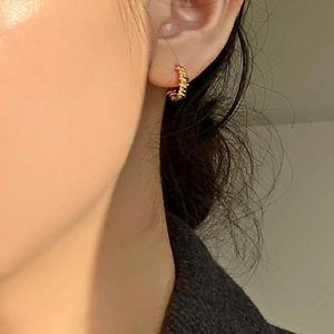 Close-up of elegant gold twisted rope hoop earring worn on female model's ear