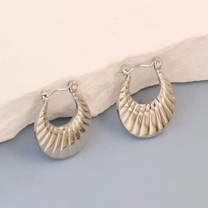 Macro detail of silver irregular geometric earrings with pleated texture on white stone