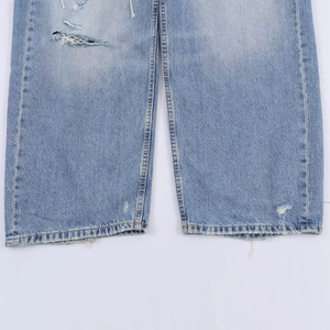 Gros plan détaillé sur la texture denim bleu clair et l'ourlet effiloché du jean en coton