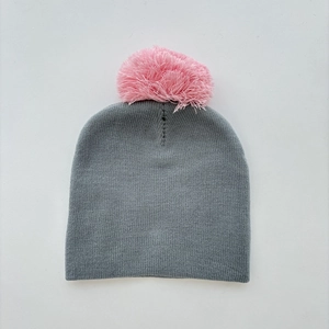 Detail of grey knitted hat featuring a vibrant pink pom-pom and thick warm textures