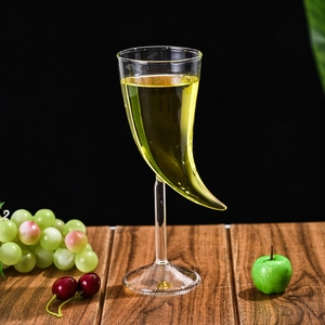 Unique horn-shaped glass cocktail goblet on a stem with yellow drink against dark background