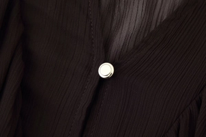 Macro shot of silver circular metal button on black pleated midi dress fabric