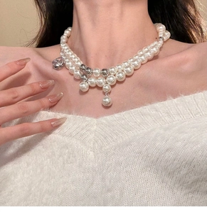 Detail of double-layer pearl necklace with zircon accents on a white plush garment