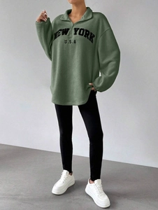 Détail du pull en polaire vert sauge avec broderie New York et col à demi-fermeture