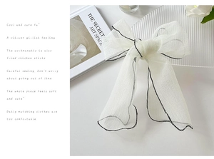 Detail of white organza bow hair clip with elegant black stitched edges and mesh texture
