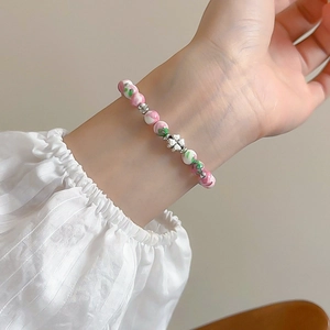 Close-up of pink and green beaded bracelet with silver four-leaf clover charm on wrist