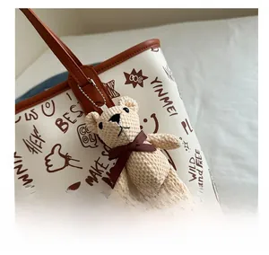 Detail of graffiti print PU tote bag featuring a cute knitted bear charm on the strap