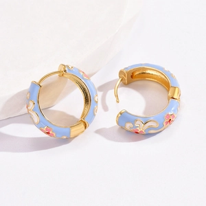 Macro detail of enamel floral earrings with blue background and gold plated finish