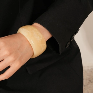 Detail of a wide resin bangle in cream beige with marbled texture on a model's wrist