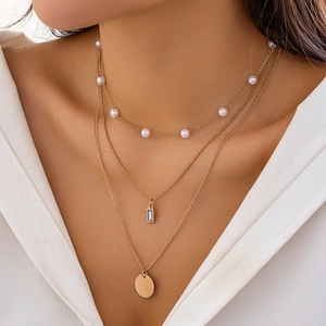 Detail shot of a layered gold necklace set with pearls and pendants on a white shirt