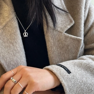 Detailed view of sterling silver twisted heart necklace and stacked rings on a model