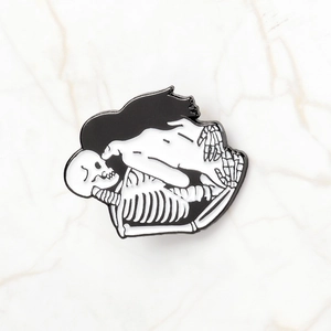 Close-up of a black and white enamel skull brooch with two skeletons on marble surface