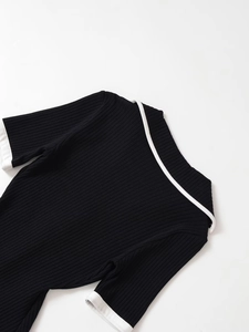 Dettaglio di abito in maglia nera con bordo bianco a contrasto su colletto e maniche