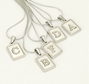 Macro detail of stainless steel snake chain necklaces with mother of pearl letter pendants