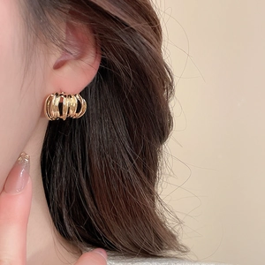 Close-up of golden multi-layer textured hoop earring worn by a model in a minimal setting