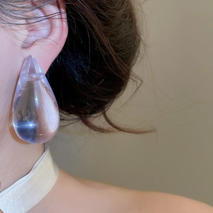 Close-up detail of a large transparent purple acrylic water drop earring on a model's ear.