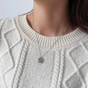 Close-up of a square silver pendant necklace with leaf texture on a white cable knit sweater