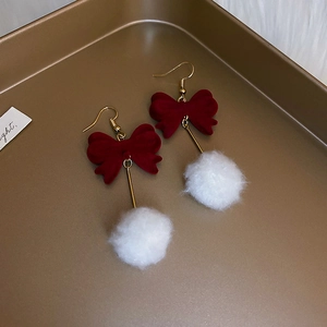 Detailed view of festive red velvet bow earrings with white fuzzy pom-poms on a gold tray