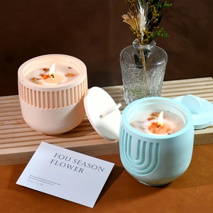 Detail of striped and U-shaped textured candle jars with dried petals on wooden tray