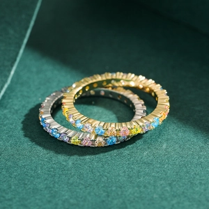 Eternity rings in gold and silver set with multi-colored gemstones on green background
