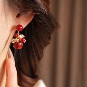 Dettaglio di orecchini a fiore con zirconi rossi placcati oro 18K indossati sul lobo