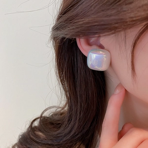 Close-up of geometric iridescent pearl stud earrings worn by a model in soft natural light