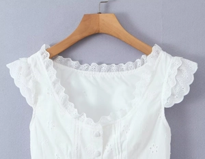 Détail du haut blanc sans manches en dentelle avec broderie et boutons dorés
