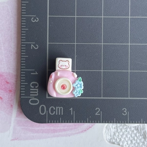 Macro shot of mini pink bear resin camera accessory showing 1.5cm size on a scale ruler