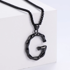 Détail du collier pendentif lettre G noir mat avec bords ondulés sur fond blanc