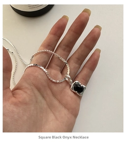 Detailed close-up of a square silver pendant with black onyx gemstone on a twisted chain