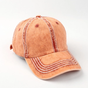 Close-up of contrast stitching on washed orange cotton baseball cap with curved brim