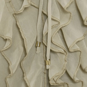 Detail of light green ruffled translucent shirt featuring tie-strings with gold beads