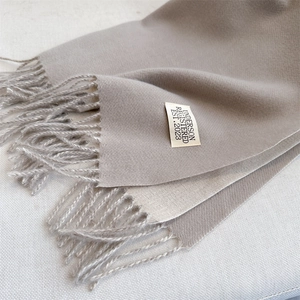 Close-up of beige cashmere-like scarf texture with fringe detail and woven brand label