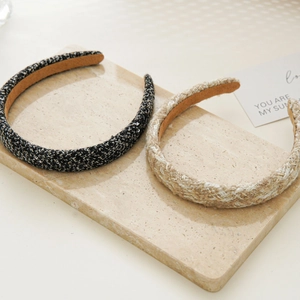 Detail view of black-gold and beige-gold tweed headbands on a marble surface