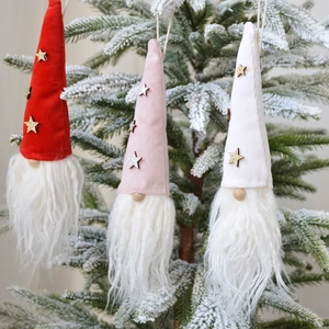 Three plush Christmas gnome hanging ornaments in red, pink, and white on a snowy tree branch