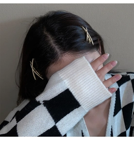 Detailed close-up of a golden X-shaped hair clip with shimmering rhinestones on hair