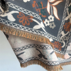 Detail showing the thick jacquard texture and orange fringes of the floral winter scarf