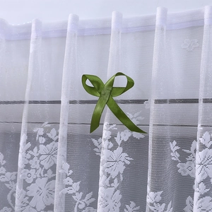 Close-up of white lace curtain with intricate floral embroidery and a green silk bow
