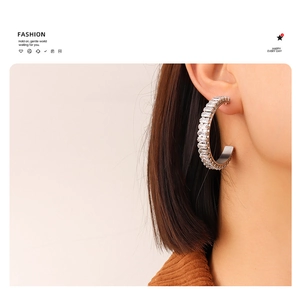 Close-up of C-shaped silver earrings with baguette-cut zircons worn by a model