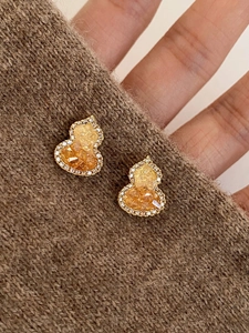Detail of gold gourd earrings with amber gemstones on a cozy brown knitted sweater