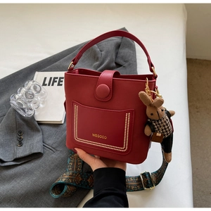 Chic red PU leather bucket bag with wide strap and rabbit charm on grey blazer