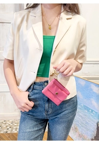 Close-up of a pink leather mini coin purse keychain held by a model in casual attire