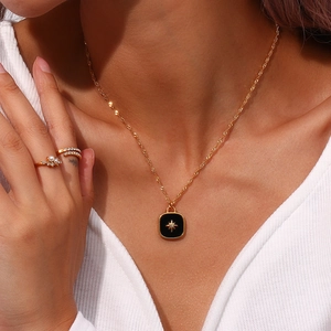 Close-up of golden necklace with black square pendant featuring a star and tiny diamond
