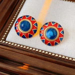Macro view of vintage enamel earrings with red patterns and a blue center gemstone